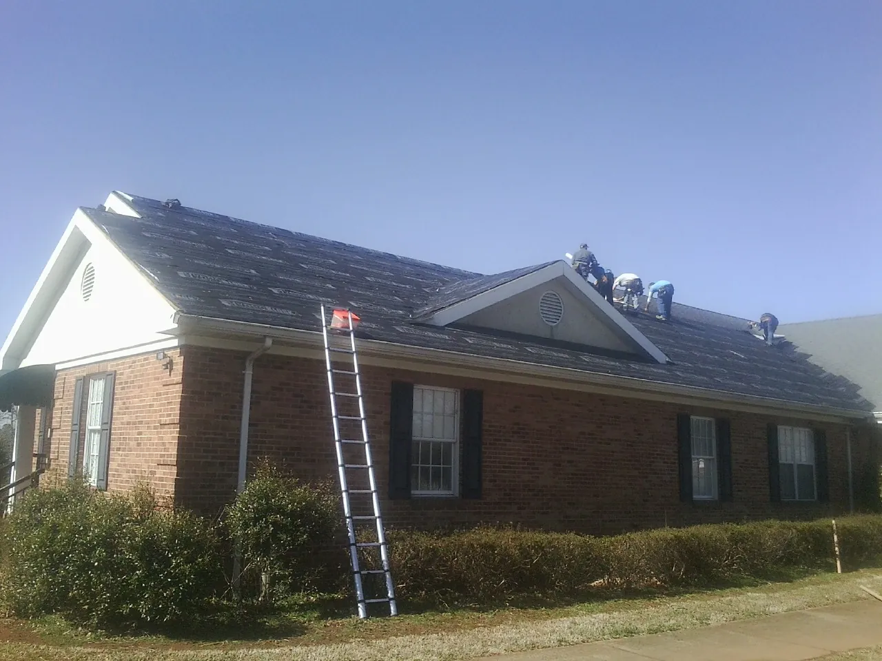 Crew tearing shingles off a brick ranch roof with a ladder set — Emergency Roof Repair work by our crew in Mccloud