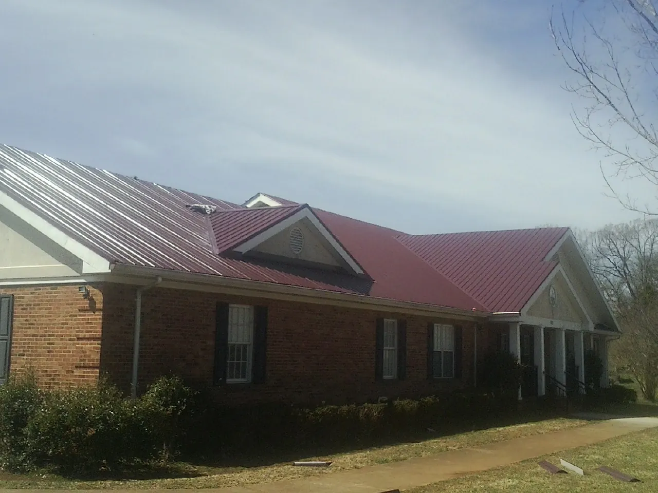 Red metal roof with gabled entries on a long brick building, from a Hail Damage Roof Repair job in Mccloud