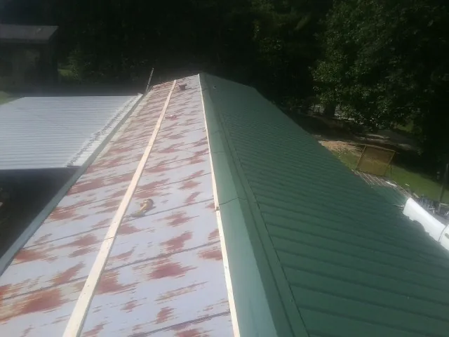 Old rusted panels beside newly installed green metal roofing — Wind Damage Roof Repair by Roofing Brothers in Mccloud