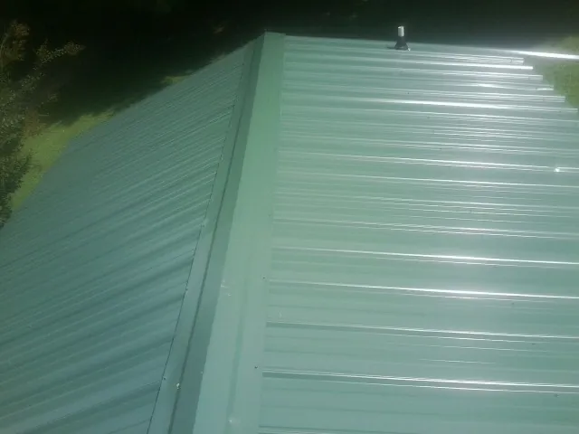 New green metal panels meeting at the ridge of a roof — Flat Roof Repair work by our crew in Mccloud