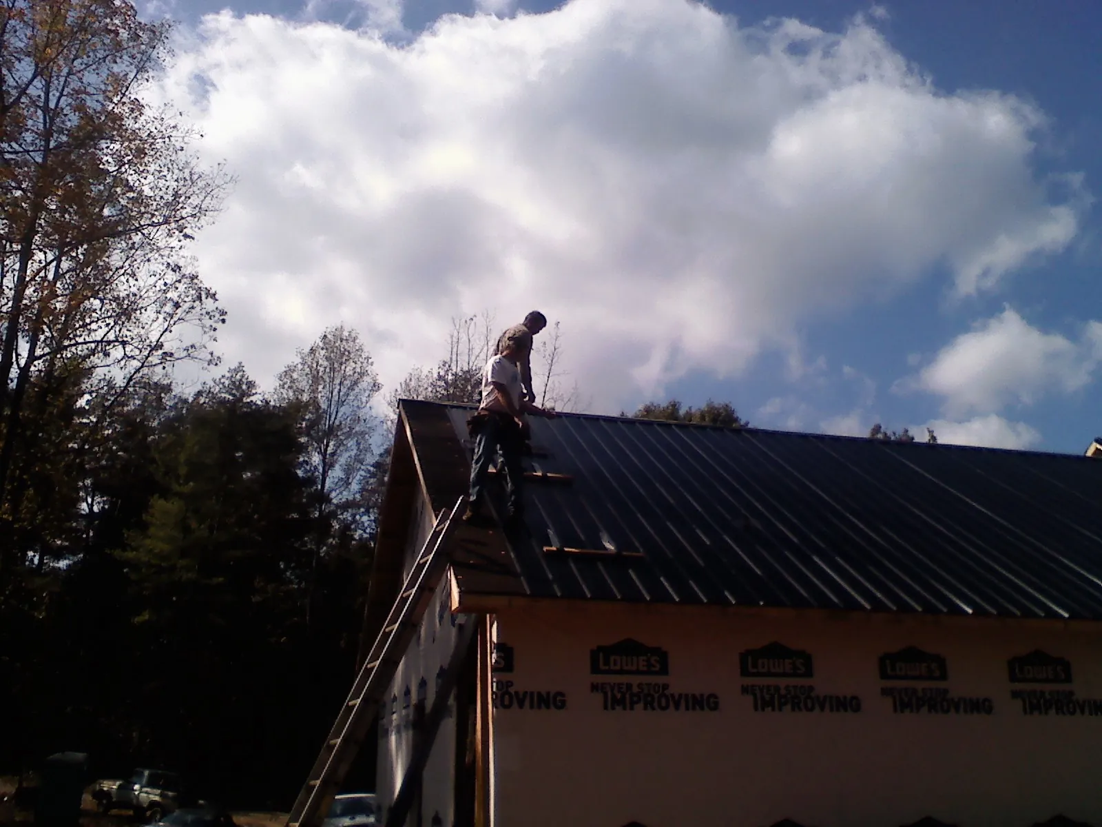 Roofer fastening dark metal panels high against a cloudy sky, from a Roof Inspection job in Mccloud