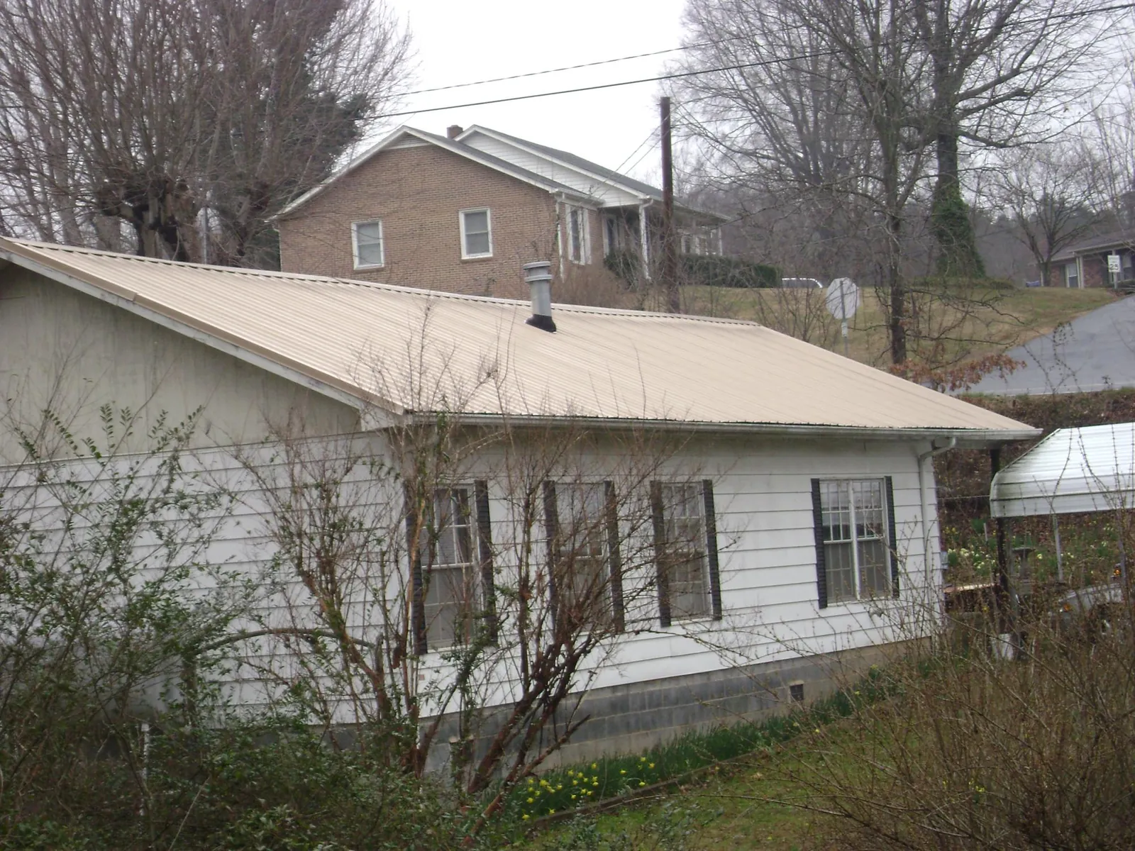 Tan metal roof on a white sided house set into a hillside — Commercial Roofing by Roofing Brothers in Mccloud